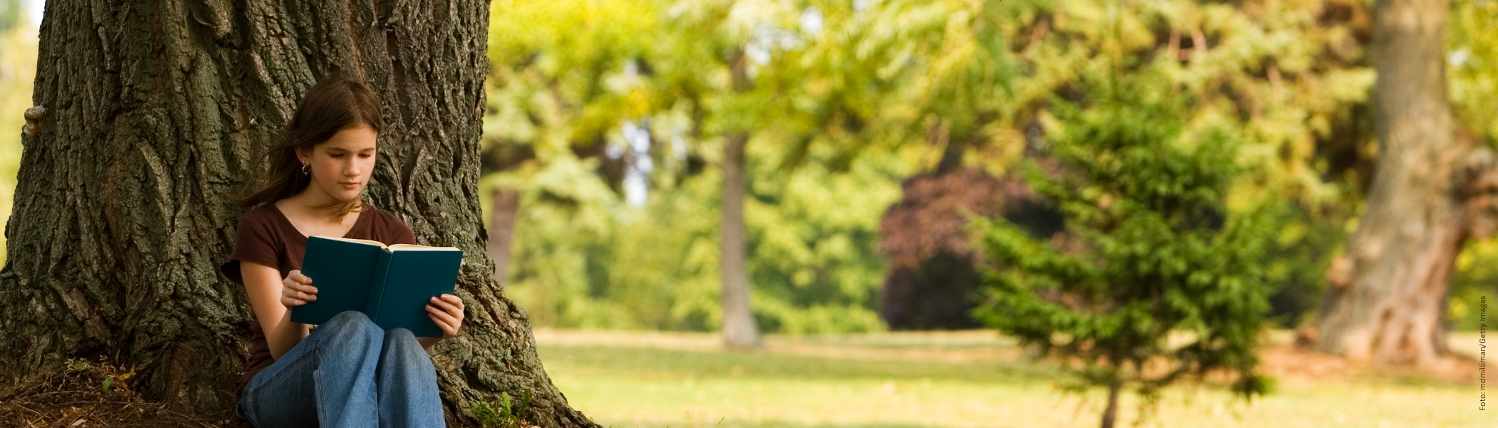 Mädchen liest an einem Baum gelehnt